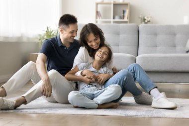 Sevgi dolu anlar. Şefkatli, şefkatli bin yıllık anne baba evde dinleniyor ergenlik çağındaki küçük kızına sarılıp gülüp eğleniyor oturma odasındaki sıcak ahşap zeminde oturmuş eğleniyor.