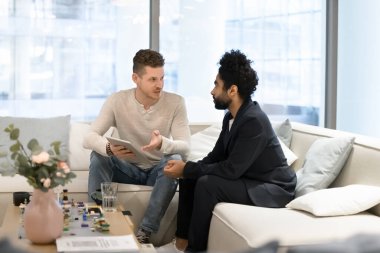 İki çok ırklı iş arkadaşı ofis koltuğunda iş görüşmeleri, tablet bilgisayarları paylaşmalar, konuşmalar. Kafkasyalı işadamı Arap yatırımcı ve ortağına çevrimiçi başlangıç projesi gösteriyor