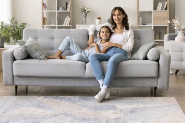 Ev konforu. Gülümseyen genç kadın anne dadı abla rahat oturma odasında kanepede otur kucağına al ergen kız küçük kız kardeş arkana yaslan şefkatli insanlarla konuş birlikte rahatla