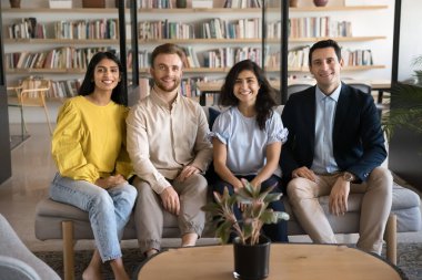 Kütüphanedeki koltukta oturup kameraya bakıp gülümseyen mutlu yetişkin öğrencilerden oluşan çeşitli bir takım. Çok ırklı iş arkadaşlarının grup portresi, iş yerinde kanepede dinlenen arkadaşlar