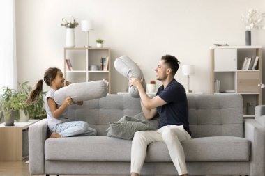 Aktif hafta sonu. Yaramaz hiperaktif küçük kız kanepede yetişkin bir adamla oynuyor baba bakıcı ağabey birlikte eğleniyor kanepe yastıklarıyla kavga ediyor komik savaş için ortopedik yastıklar kullanıyor