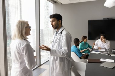 Genç erkek doktor çok ırklı klinik personeli hastane yönetim kurulundaki yaşlı bayan meslektaşla konuşuyor. Orta yaşlı akıl hocasıyla tıbbi stajyer konuşması. Tecrübeli bir doktor. Teşhis hakkında danışmanlık yap.