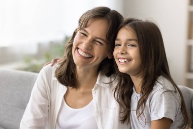 Sıkı aile bağları. Portre neşeli genç yetişkin kadın koruyucu anne küçük ergen kız evlat edinilmiş kız oturma odasındaki rahat kanepede sarılıyor başları yan yana.