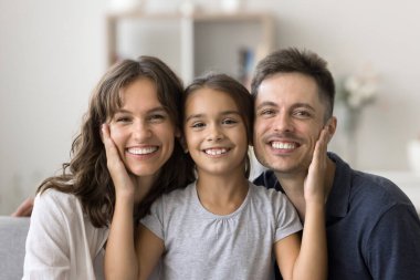 Sevgi dolu bir aile. Neşeli gülümseyen ebeveynlerin portresi. Çocuk evde, koltukta sarılıyor. Sevimli küçük kız, şefkatli yüzler okşuyor. Sevgili bin yıllık anne babasının kameraya bakarken yanaklarına dokunuyor.