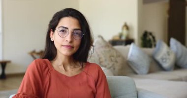 Ön yüzü yakın, mutlu 30 'lu yaşlarda Brezilyalı bir kadın gözlük takıyor beyaz dişli içten bir gülümseme takıyor oturma odasındaki koltukta oturan kameraya bakıyor. Ev sahibi portresi, ev eğlencesi