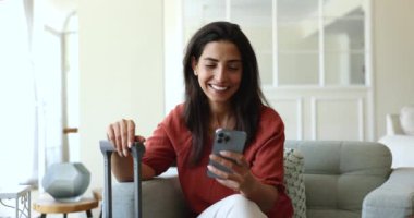 Akıllı telefon kullanan bir kadın bavul tutarken, seyahat planlarken, rezervasyon, otel, ulaşım, iş seyahatine hazırlanırken, seyahat rehberlerini kontrol ederken, mobil uygulama kullanarak taksi çağırırken,