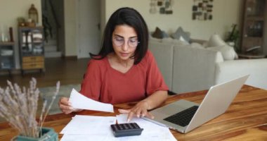 Mali durumunu idare eden kadın, dizüstü bilgisayar, hesap makinesi ve belgelerle masada oturmaktan memnun. Hesabını uzlaştırmak, bütçede olumlu sonuçlar bulmak. Finansal okuryazarlık, faturaları ödemek için yeterli para.