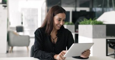 Gülümseyen Arap ofis çalışanı, iş belgelerine ve dosyalara erişmek ve işbirliği yapmak için bulut depolama uygulamalarını kullanarak masasında oturuyor, işle ilgili görevler için bilgi toplamak için interneti tarıyor.