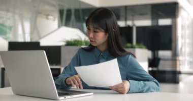 Ofiste çalışan Asyalı bir kadın, dizüstü bilgisayar, inceleme kağıtları kullanıyor, finansal raporlar hazırlıyor, şirket performansını analiz ediyor ve bütçelerini planlıyor, proje planlarına hazırlanıyor, ilerlemeyi takip ediyor, ayarlamalar yapıyor