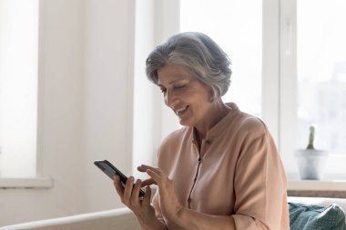 Gülümseyen yaşlı bir kadın kanepeye oturur, cep telefonuyla başvuru yapar, arkadaşlarıyla çevrimiçi sohbetin tadını çıkarır, yeni cep telefonu yazılımları öğrenir. Eski nesil ve sosyal medya, kablosuz teknoloji, sanal servis kullanım kavramı