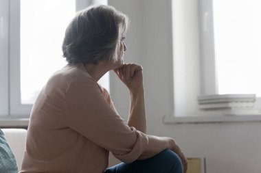 Ciddi 50 'li yaşlarda kadın pencereden dışarı bakar evde yalnız zaman geçirir, üzgün ya da hayal kırıklığına uğramış hisseder, evde oturan birini bekler ya da özler. Yalnızlık, emeklilik yalnızlığı, nostaljik ruh hali konsepti.