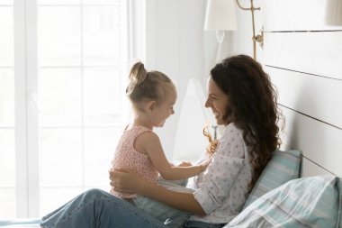 Neşeli, mutlu bir anne kucağında küçük tatlı bir kız çocuğu, gülüyor, kızıyla eğleniyor, anneliğin tadını çıkarıyor, aile eğlencesi, yatak odasında dinleniyor.