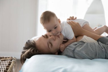 Sevgi dolu yeni anne kucağında bebek, yatakta uzanmış, kapalı gözlerle sevimli çocuğu öpüyor, çocuk bakımı, annelik, ebeveynlik, şefkatli, şefkatli çocuğu okşuyor.