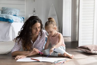 Anne küçük çocuğu yaratıcı bir hobiye yönlendiriyor, evdeki ısıtma tabanında dinleniyor, renkli kalemlerle kağıt albüm çiziyor, konuşuyor, aile tatilini geçiriyor, kızıyla hafta sonu geçiriyor.