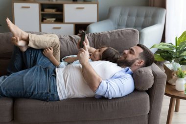 Mutlu tembel baba ve oğul kanepede birlikte dinleniyor, cep telefonunda daktilo çekiyor, internetten alışveriş yapıyor, selfie çekiyor, video görüşmesi yapıyor, cep telefonu ekranına bakıyor, gülümsüyor, gülüyor, eğleniyor.