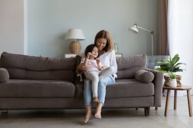 Mutlu bir anne kucağında tatlı küçük kızını kucağında tutuyor, sevgi, ilgi, şefkat dolu bir çocuğa sarılıyor, kanepesinde çocuğunu gıdıklıyor, kızla oynuyor, gülümsüyor, gülüyor, aile eğlencesine gülüyor, annelik yapıyor.