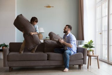 Mutlu küçük çocuk ve neşeli baba evde aktif oyunlar oynuyor, kanepede yastık sallıyor, eğleniyor, aile eğlencesi, babalık, çocukluk. Tam uzunluk