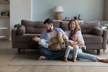 Heyecanlı, neşeli ebeveynler sıcak zeminde enerjik küçük çocukları gıdıklıyor, gülüyor, eğleniyor, evde aile aktivitelerinden keyif alıyorlar. Mutlu anne ve baba kıkırdıyor, bağırıyor. Oğlan ve kız çocukları.