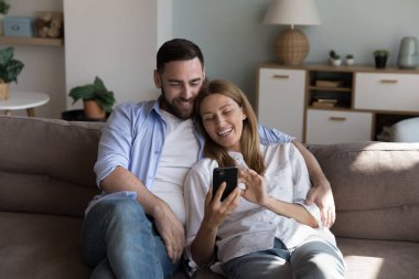 Mutlu sevgili çiftler evlerinde kanepede dinleniyorlar, online uygulama kullanıyorlar, akıllı telefondan sanal servis kullanıyorlar, internetten alışveriş yapıyorlar, otel tutuyorlar, sipariş veriyorlar, gülüyorlar.