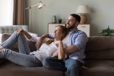 Mutlu, hayalperest bir çift, boş zamanların tadını çıkarıyor, rahat bir evde dinleniyor, kanepede uzanıyor, düşünüyor, hayal kuruyor, birlikte plan yapıyor, gülümsüyor, konuşuyor, pencereden dışarı bakıyor, sarılıyor.