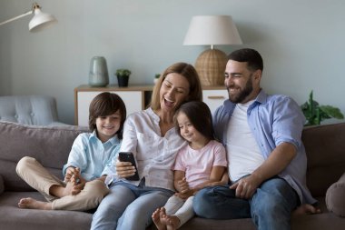 Mutlu ebeveynler ve çocuklar akıllı telefondan video konuşmaları, kanepe üzerinde komik selfie fotoğrafları çekmeleri, cep telefonu tutmaları, gülümsemeleri, ekrana gülmeleri, iletişimin tadını çıkarmaları.