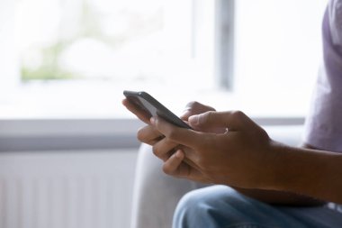 Yakın çekim Afrikalı adam elleri modern akıllı telefon tutuyor evdeki kanepede oturuyor. Elektronik hizmet alıcısı, perakende e-ticaret istemcisi, mal satın alma, internette arama bilgileri, e-randevu kavramı