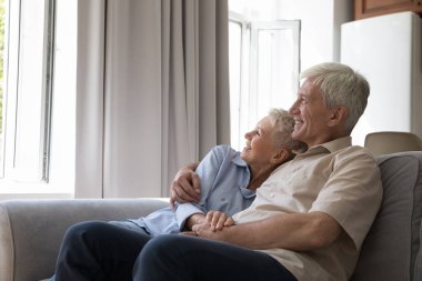 Gülen yaşlı, gri saçlı, aşık bir çift. Hayal kuran, pencereden dışarı bakan rahat koltukta rahat rahat sohbet eden, modern evde boş vakit geçiren bir çift. Mutlu evlilik, uyum, romantik ilişkiler konsepti