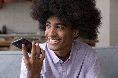 Afrikalı adam telefon eder, kanepede oturur, akıllı telefondan konuşur, uzaktan hoş sohbetler eder, sesli mesaj bırakır, mobil uygulama aracılığıyla ses gönderir, modern teknoloji kavramını kullanır.