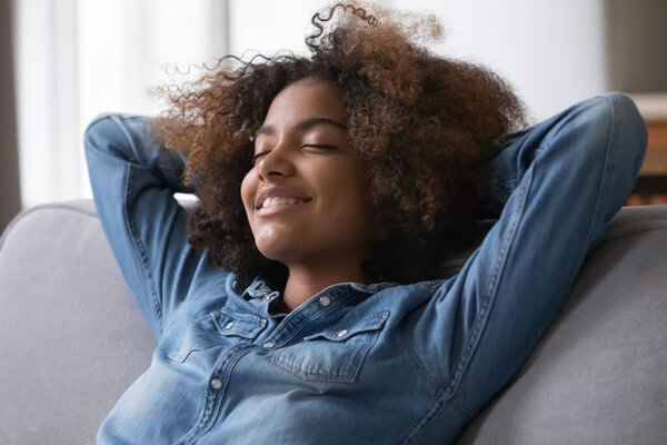 Close up beautiful peaceful African teenage girl relaxing alone at modern home breathing fresh conditioned air in cozy warm living room. Enjoy stress free weekend, repose, healthy daytime nap concept