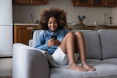 Şirin Afrikalı genç kız akıllı telefonuyla kanepede oturur, arkadaşlarıyla mesajlaşır, sosyal ağlarda sohbet eder, internet kullanarak yeni mobil uygulamaların tadını çıkarır. Genç nesil modern kablosuz teknoloji kullanıyor, eğlenceli konsept