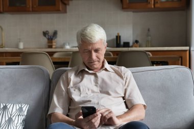 Gri saçlı adam kanepeye oturur, akıllı telefon kullanır, yetişkin çocukları arar, internette vakit geçirir, arkadaşa mesaj atar, mesajlaşır. Eski ve modern kablosuz teknoloji, kolay, konfor kullanımı konsepti