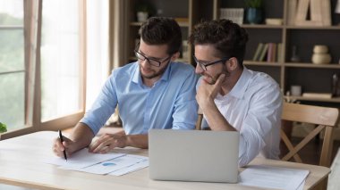 Aile içi iş projesinde çalışan pozitif nişanlı ikiz kardeşler iş yerindeki kağıt pazarlama raporlarını dizüstü bilgisayarla tartışıyor, konuşuyor, gülümsüyor, satışları analiz ediyorlar.