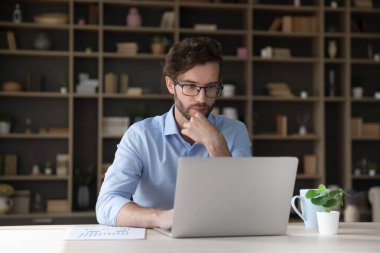 Laptop bilgisayarında çalışan odaklanmış genç bir iş adamı. İş için modern internet teknolojisini kullanan serbest iş projesini düşünen, çeneye dokunan, ekrana bakan serbest çalışan biri.