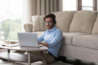 Odaklanmış, kablosuz kulaklık takan, bilgisayarını kullanan, evden online eğitim için kitap okuyan, öğrenim konferansında konuşan, Webinar izleyen, video çağrısında konuşan pozitif genç bir öğrenci.