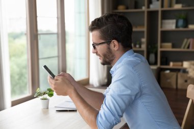 İş iletişimi için akıllı telefonu kullanan, çalışma masasında oturan, cep telefonuyla yazan serbest çalışan genç bir iş adamı. İnternette profesyonel sohbet, destek verme, internet danışmanlığı