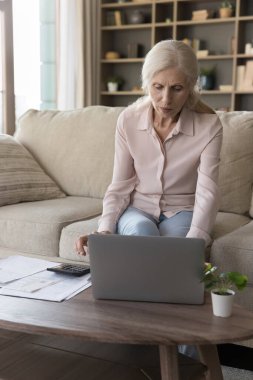 Laptop kullanan olgun bir bayan, evde hesap makinesi, yerli faturaları ödemek, bütçe kontrolü, faturalar, sayım vergileri, harcamalar, tasarruflar, online finansal uygulama
