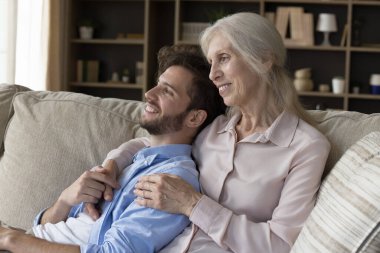 Neşeli büyük anne, genç yetişkin torunu evinde kucaklıyor, aile toplantısından zevk alıyor, boş vakitlerde el ele tutuşuyor, gülümsüyor, gelecekle ilgili planlar kuruyor, başka yere bakıyor.