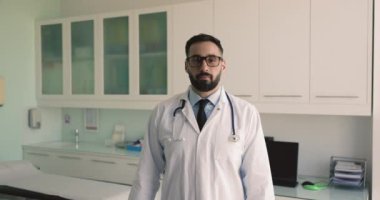 Beyaz önlüklü İspanyol pratisyen adam kolları bağlı olarak işyerinde tek başına poz veriyor, özel klinikte kariyer gelişimi ve profesyonel başarılardan memnun. Tıp çalışanı portresi