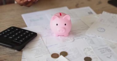 Masada oturan Afrikalı bir kadının yakın plan görüntüsü pembe kumbaraya bozuk para koyar, gelecek için para biriktirir, yarını düşünür, yatırım yapar. Bütçe, finansal okur yazarlık, tutumluluk.