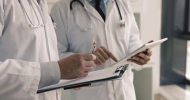 Beyaz önlüklü iki doktoru kapatın. Öncü konuşma pano ve tablet tutun, hasta semptomlarını gözden geçirin, tanı testlerini analiz edin, tedavi seçeneklerini, ilaç tedavilerini ya da potansiyel ameliyatları tartışın.