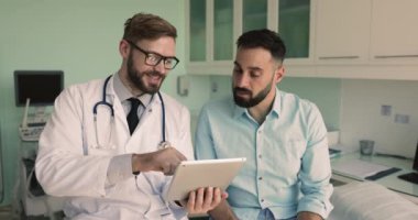 Avrupalı erkek pratisyen hekim hastaya dijital tablet ekranda test sonuçları gösteriyor, check-up sonuçlarını, sağlık taramasını, özel klinikteki randevuyu açıklıyor. Sağlık, teknoloji.