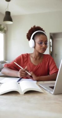 Çekici genç Afrikalı kadın kulaklık takıyor çevrimiçi öğretmenle konuşuyor, egzersiz yapıyor, üniversite ödevini hazırlıyor, okuyor, internette e-öğreniyor. Modern teknoloji, bilgi gelişimi, eğitim