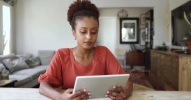 Tablet kullanan güzel Afrikalı kadın oturma odasında oturmuş sohbet ediyor, alışveriş yapıyor, pazar başvurusu üzerinden elektronik servisleri seçiyor, platformlarda videolar izliyor, internette vakit geçiriyor.