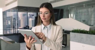 Gülümseyen profesyonel kadın modern ofiste dijital tablet kullanıyor, belgeyi gözden geçiriyor, hazırlıyor, düzenliyor, çevrimiçi sunum geliştiriyor, uzaktan iletişimi yönetiyor, yeni iş uygulaması kullanıyor