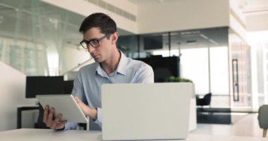 Ofiste çalışan Avrupalı işadamı, dizüstü bilgisayardaki e-posta ve iletişimi yönetirken, proje yönetimi için tablet, araştırma yapmak, iki aygıttaki çevrimiçi kaynaklara erişim
