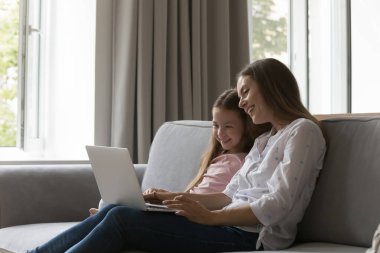 Neşeli anne ve küçük çocuk dizüstü bilgisayar başında eğleniyorlar, film izliyorlar, sitcom izliyorlar, çizgi film animasyonları yapıyorlar, online öğrenme uygulamalarını kullanıyorlar, gülüyorlar, video konuşmaları yapıyorlar, alışveriş yapıyorlar.