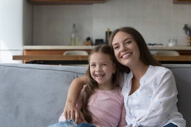 Sevgi dolu genç bir anne, neşeli küçük bir kıza sarılıyor, neşe, şefkat, sevgi, annelik, eğlence, sıcak aile ilişkisi yaşıyor, kameraya bakıyor, gülümsüyor.