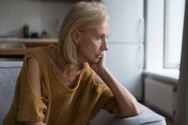 Depresyondaki olgun sarışın kadın mutsuz, hayal kırıklığına uğramış, hayal kırıklığına uğramış bakışlarla pencereye bakıyor sağlık sorununu, yalnızlığı düşünüyor. Üzgün, hayal kırıklığına uğramış bir kadın evinde samimi bir portre çiziyor.