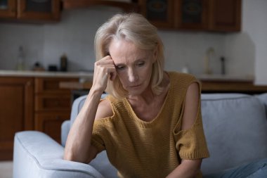 Çaresiz, üzgün, olgun, 50 'li yaşlarda bir kadın kötü haber alıyor, evinde koltukta oturuyor, hayal kırıklığı, yas, keder, sağlık, zihinsel bozukluk, kanser hastalığı, bunama yaşıyor.