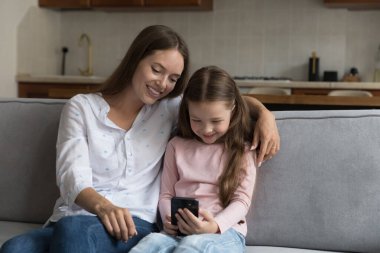 Mutlu genç dadı kadın cep telefonuyla oyun oynayan Z jenerasyonunu izliyor. Neşeli anne ve kızı evdeki kanepede dinleniyor, internetten öğrenme uygulaması kullanıyor.